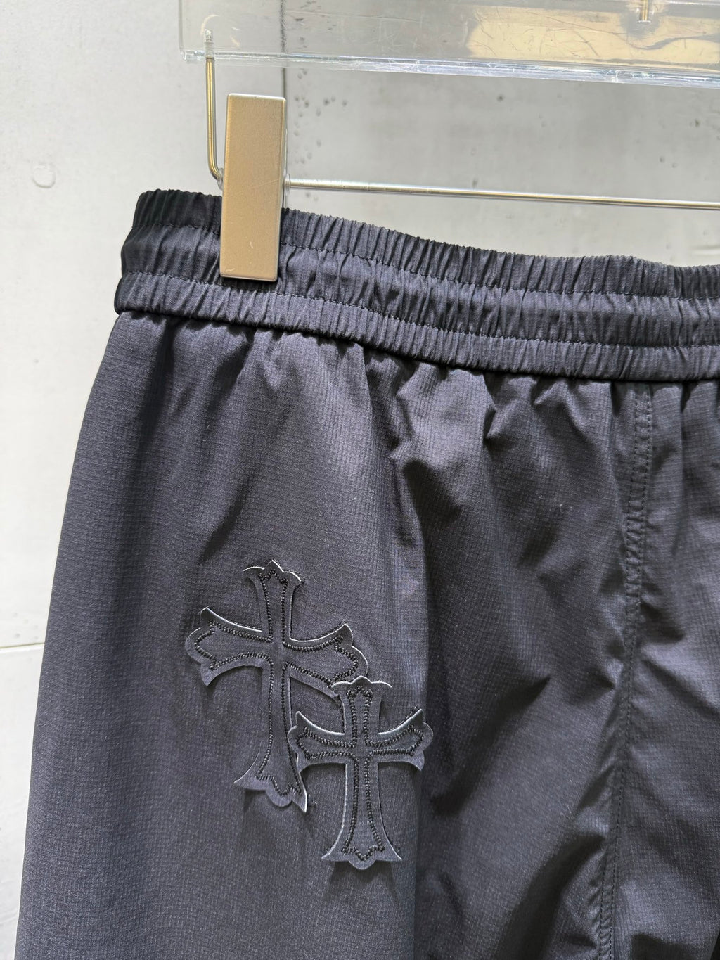 Chrome pants with large raised cross emblem on dark fabric, elastic waist.
