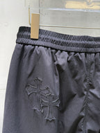 Chrome pants with large raised cross emblem on dark fabric, elastic waist.