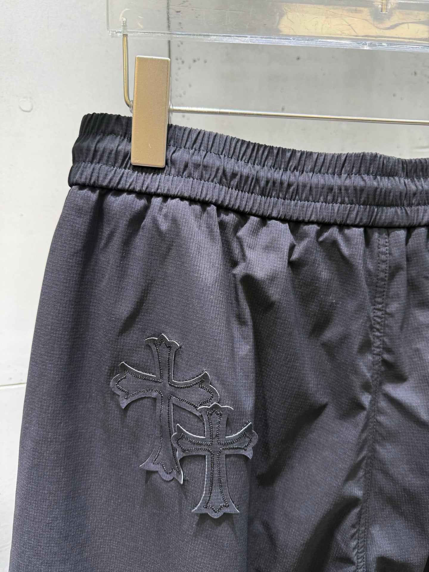 Chrome pants with large raised cross emblem on dark fabric, elastic waist.