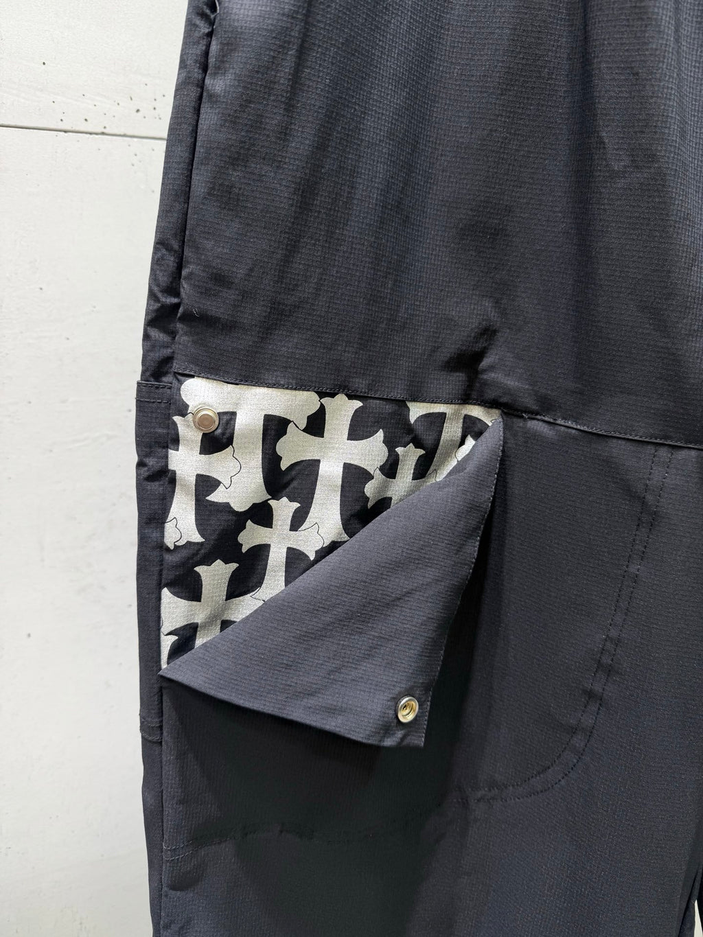 Chrome pants side pocket with button flap and geometric patch detail, dark fabric.