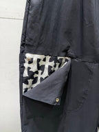Chrome pants side pocket with button flap and geometric patch detail, dark fabric.