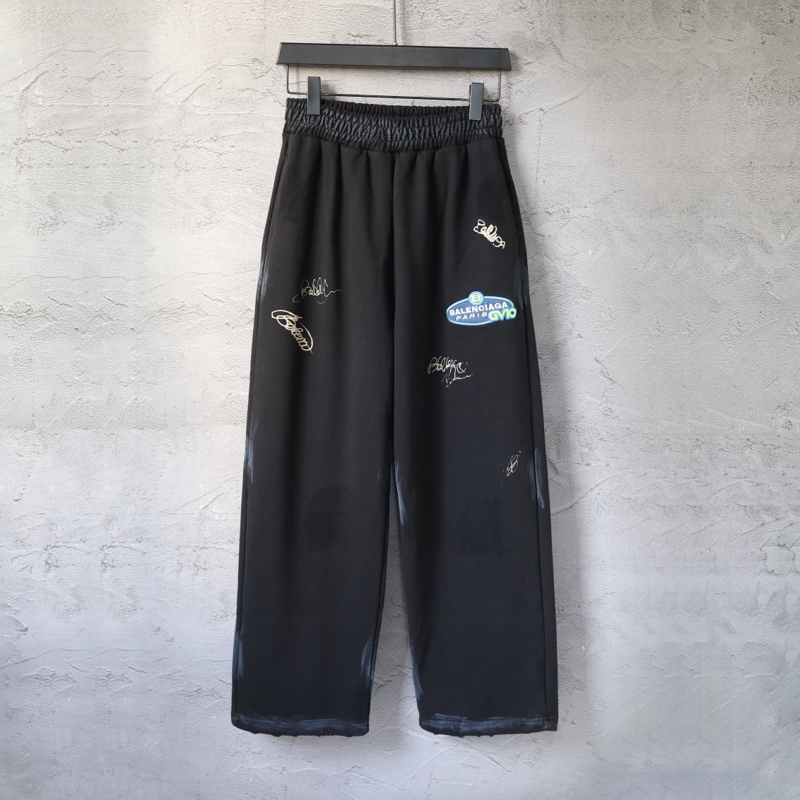Black wide-leg pants with elastic waistband and small embroidered logo marks on legs