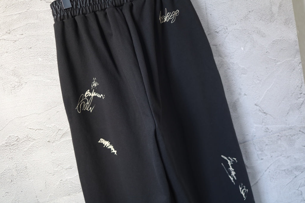 Close-up of black wide-leg pants with embroidered logo marks on the thigh