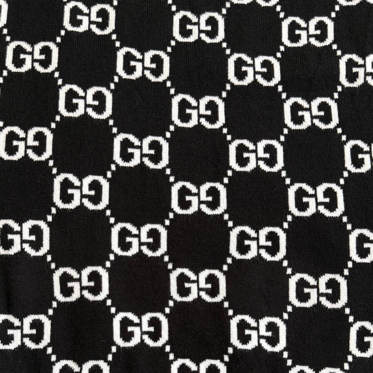 Black knit fabric with repeating white GG logo lattice pattern