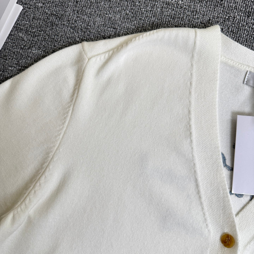White cardigan sweater shoulder and ribbed neckline, gold button partially visible