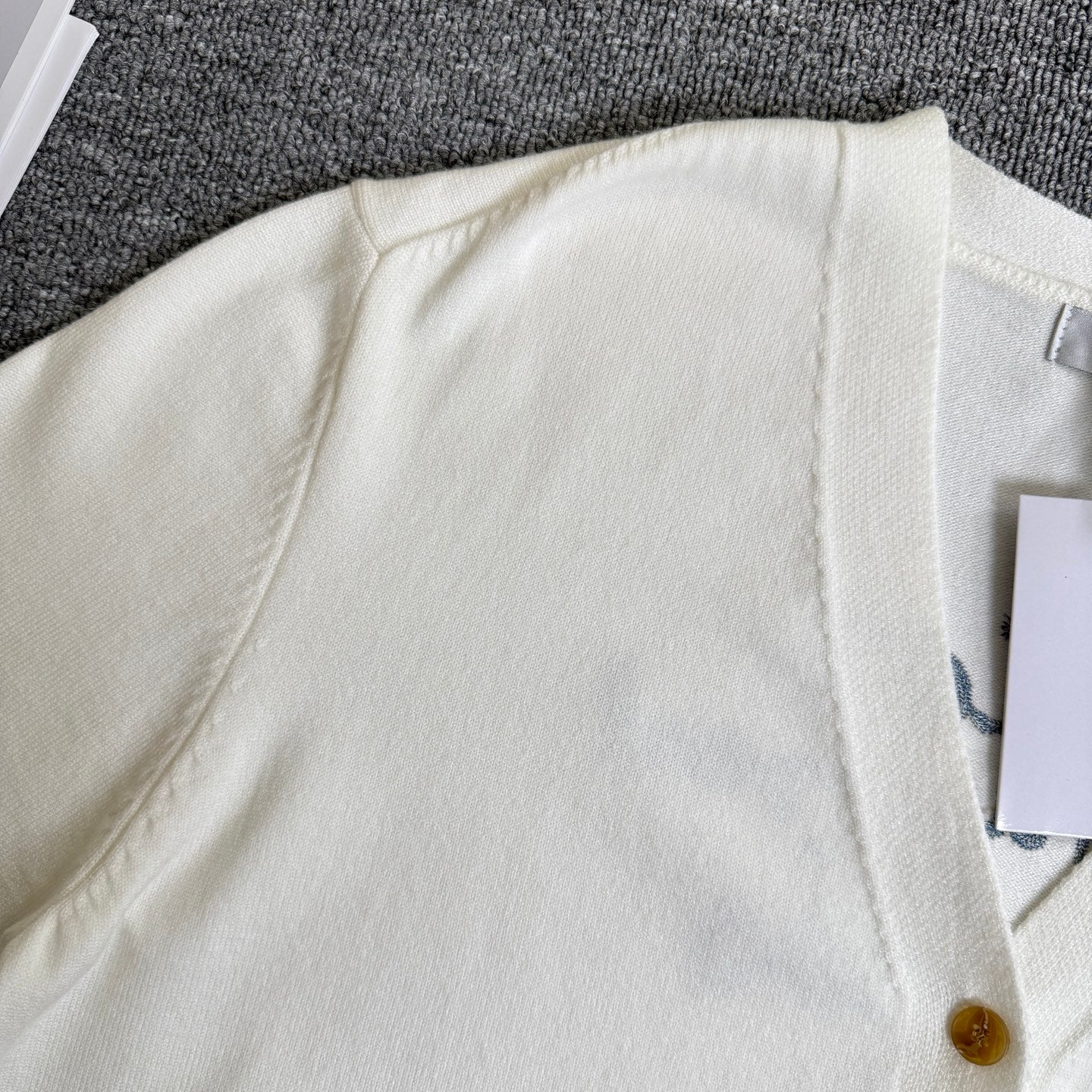 White cardigan sweater shoulder and ribbed neckline, gold button partially visible