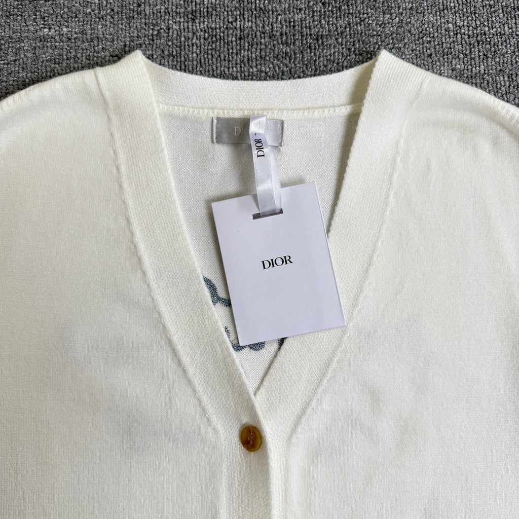 White knit cardigan sweater with V-neck trim, gold buttons, and hanging tags at front