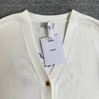 White knit cardigan sweater with V-neck trim, gold buttons, and hanging tags at front