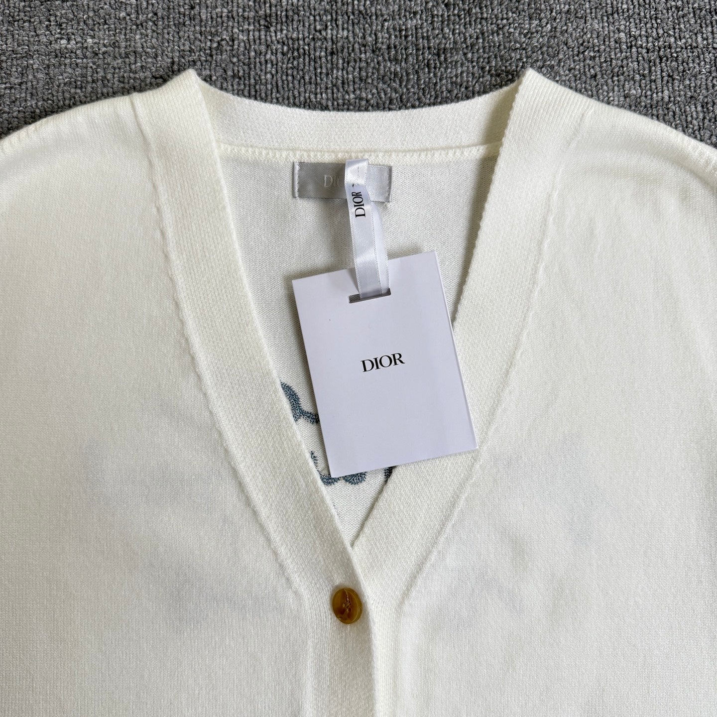 White knit cardigan sweater with V-neck trim, gold buttons, and hanging tags at front