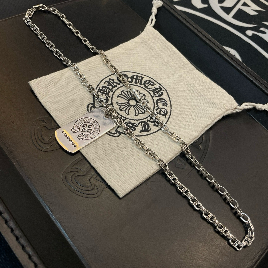 Silver-tone chain necklace with two pendants laid over fabric pouch
