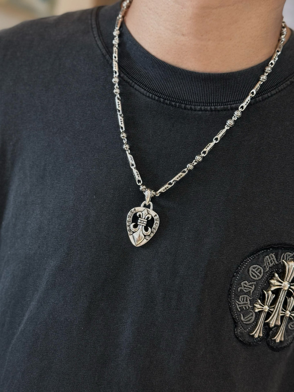 Silver-tone chain necklace with heart pendant on dark crewneck T-shirt neckline
