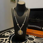 Silver-tone chain necklace with round pendant featuring a gold cross on a black stand
