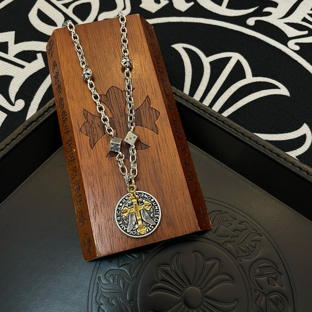 Silver-tone chain necklace with round pendant and gold cross on a wooden display block