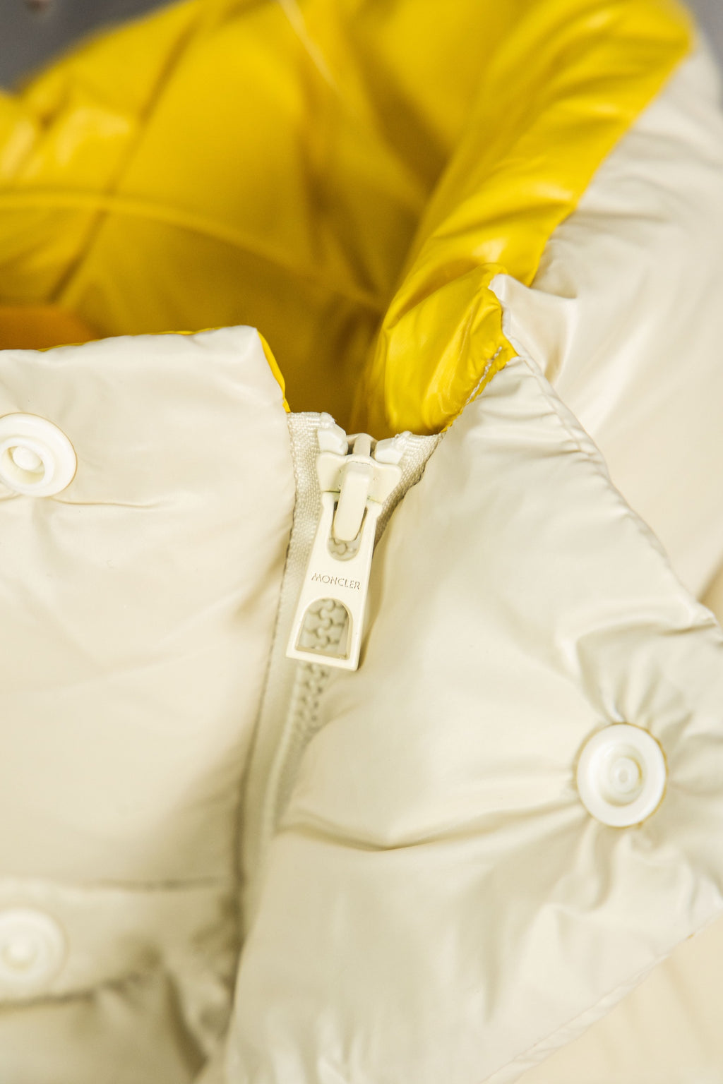 Cream puffer jacket with snap buttons at shoulder and visible zipper tag