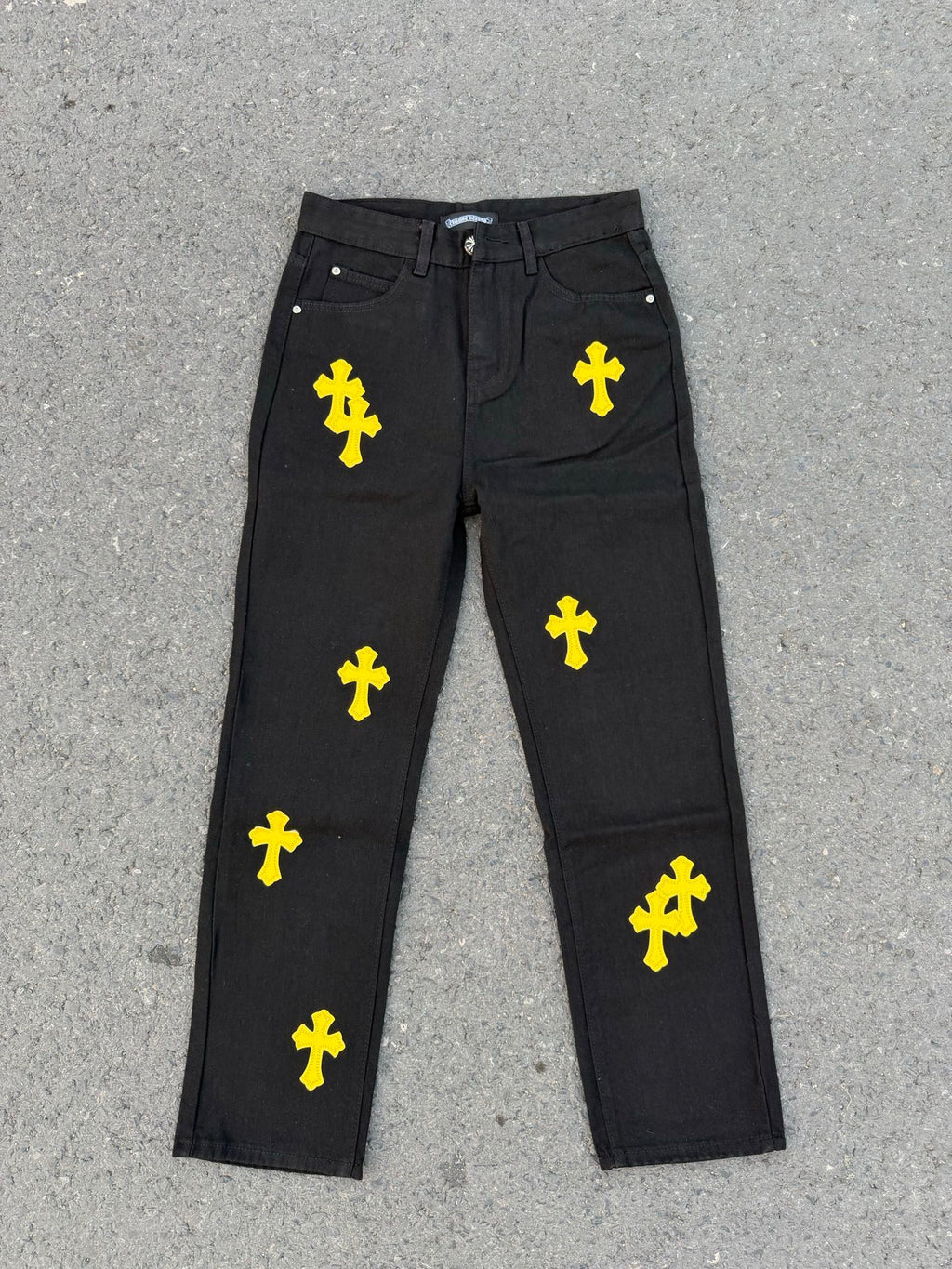 Chrome pants in dark fabric with repeating yellow cross graphics across the legs