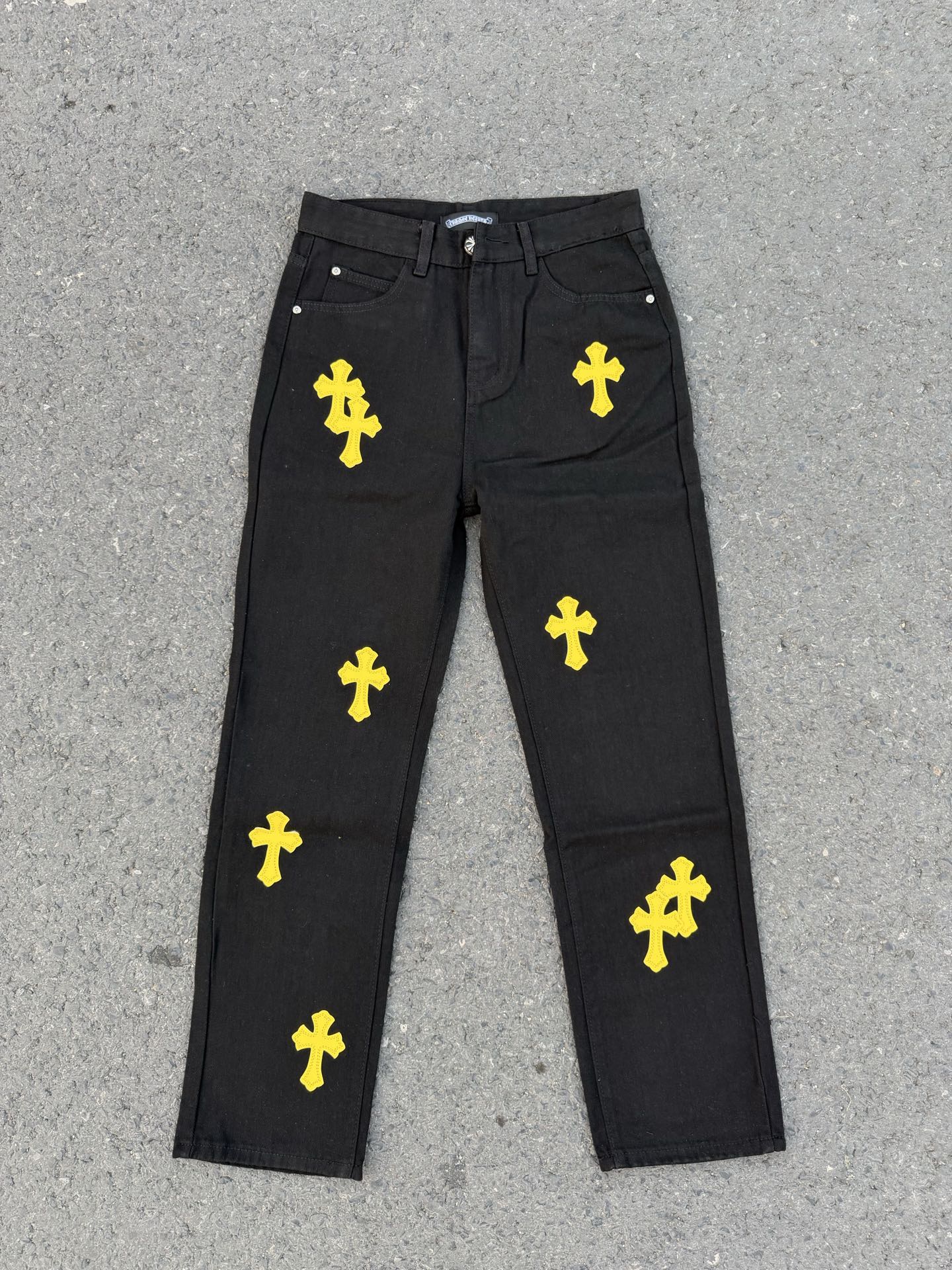 Chrome pants in dark fabric with repeating yellow cross graphics across the legs