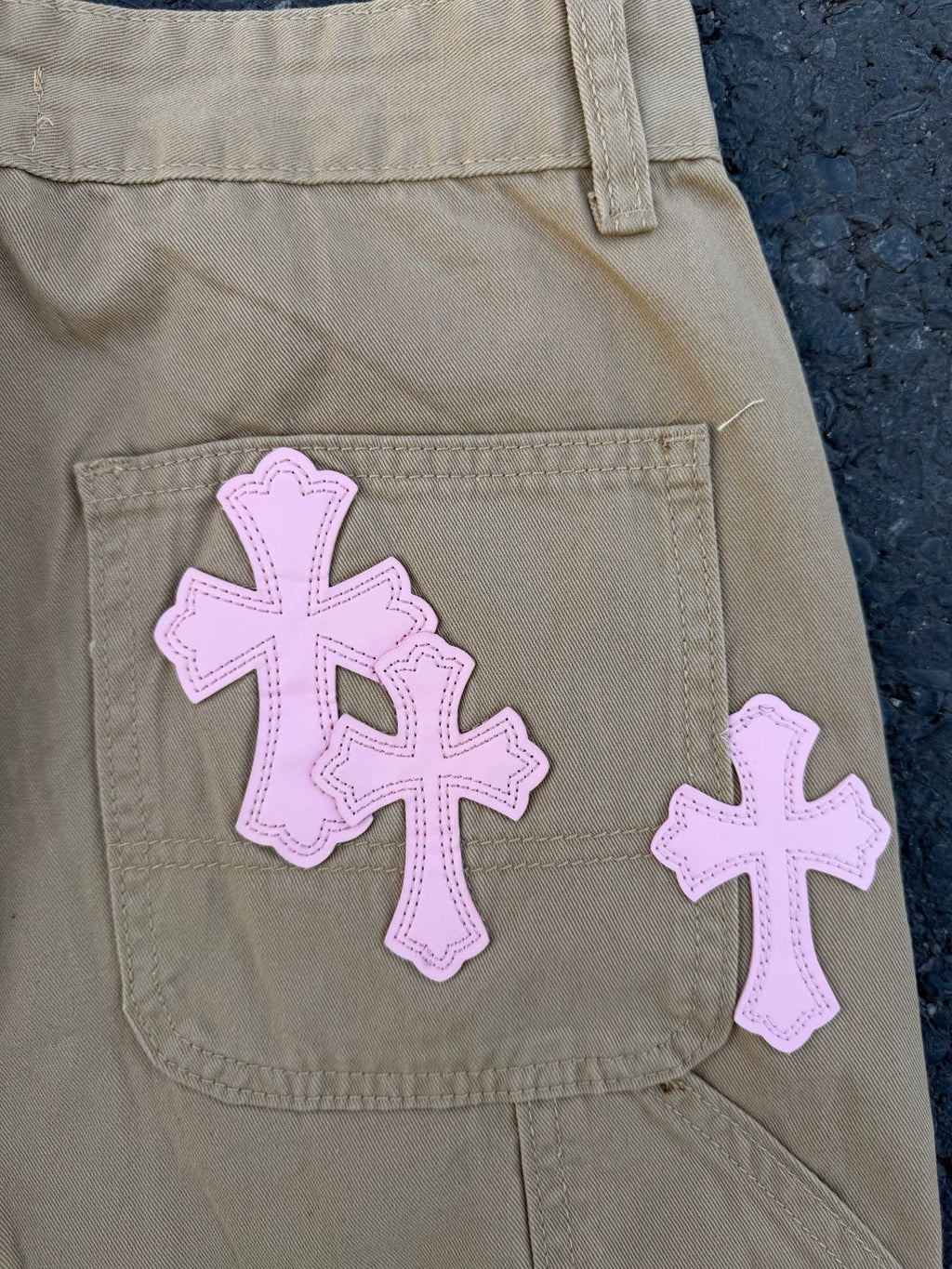 Beige pants close-up of side pocket with large purple cross appliqué