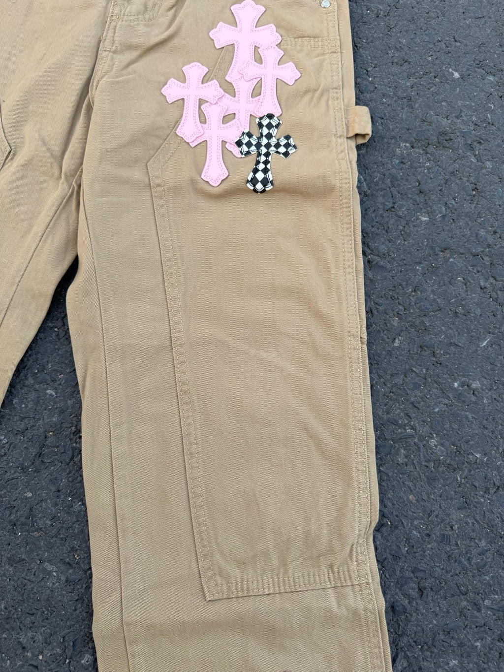 Beige pants with pink and black-checkered cross appliques on front pocket