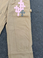 Beige pants with pink and black-checkered cross appliques on front pocket