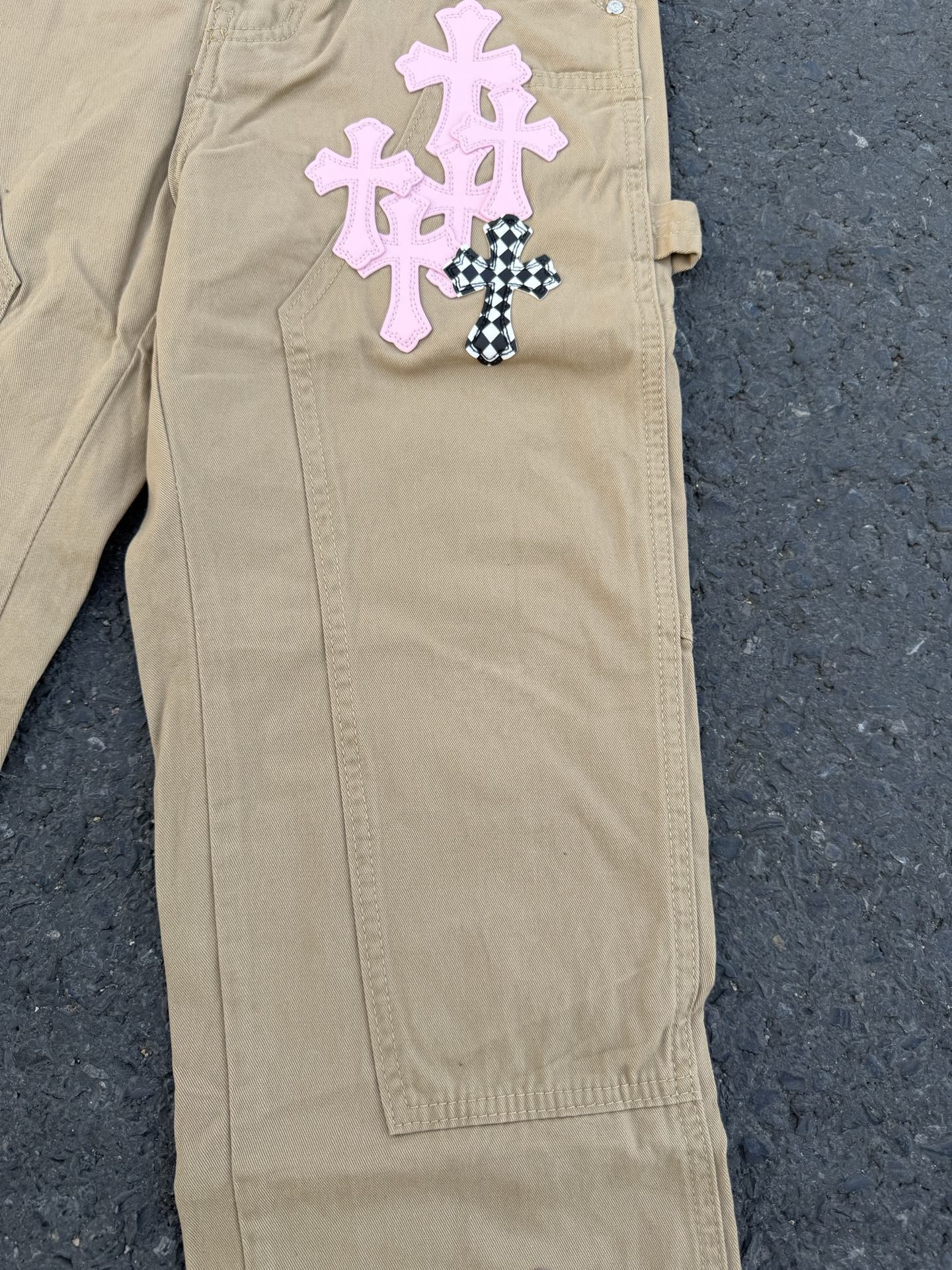 Beige pants with pink and black-checkered cross appliques on front pocket