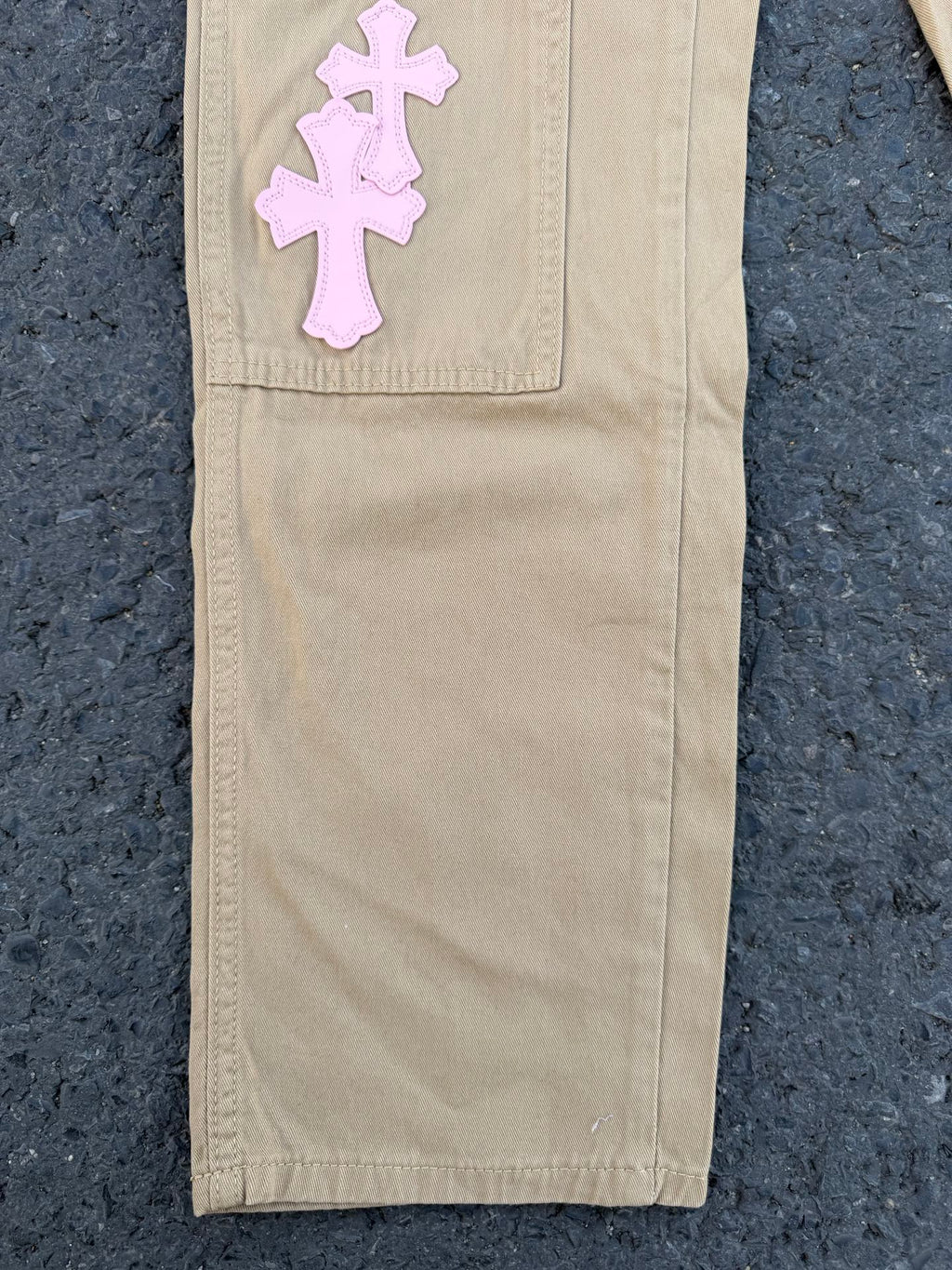 Beige pants with large pink cross applique on upper leg