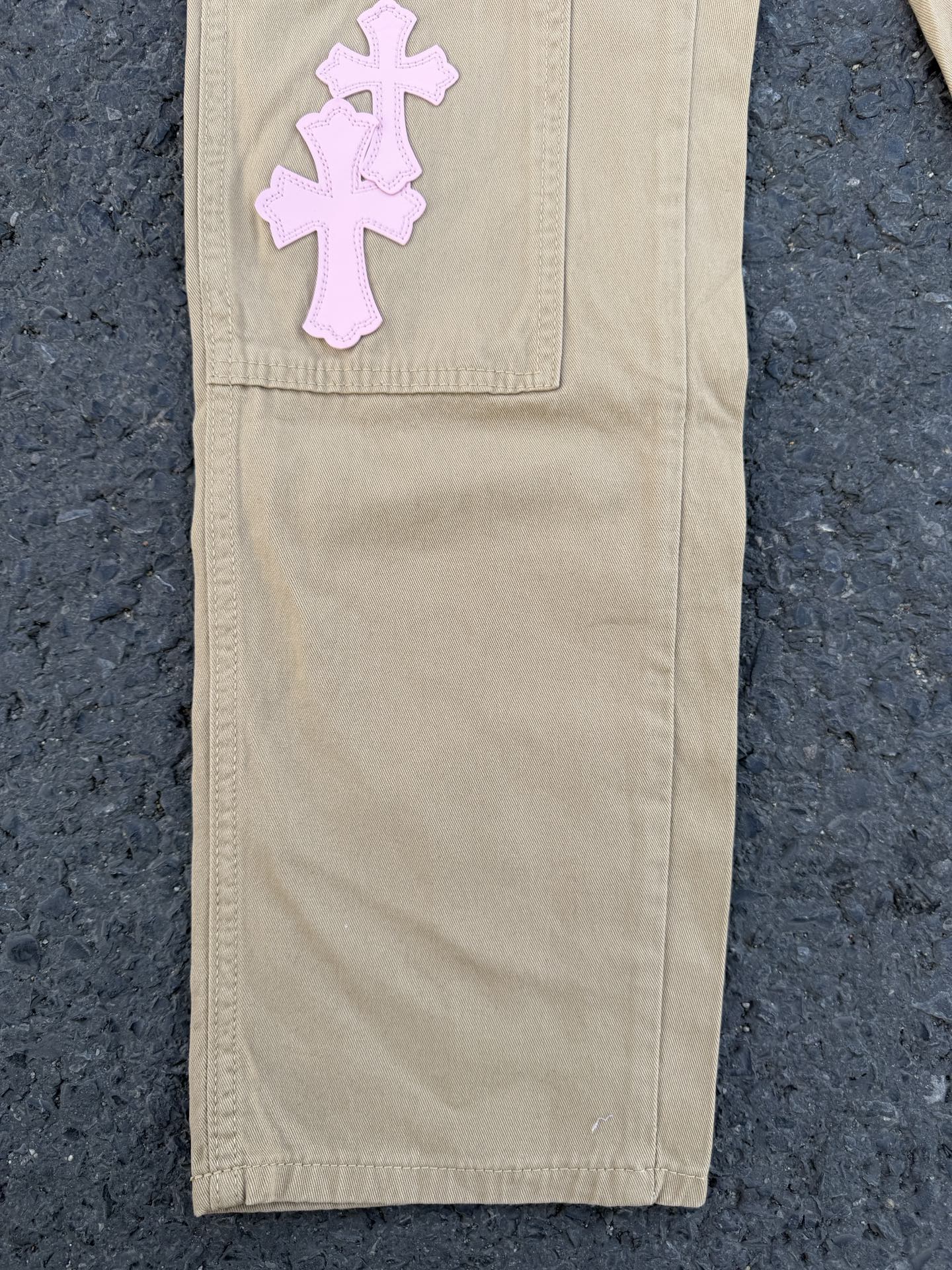 Beige pants with large pink cross applique on upper leg