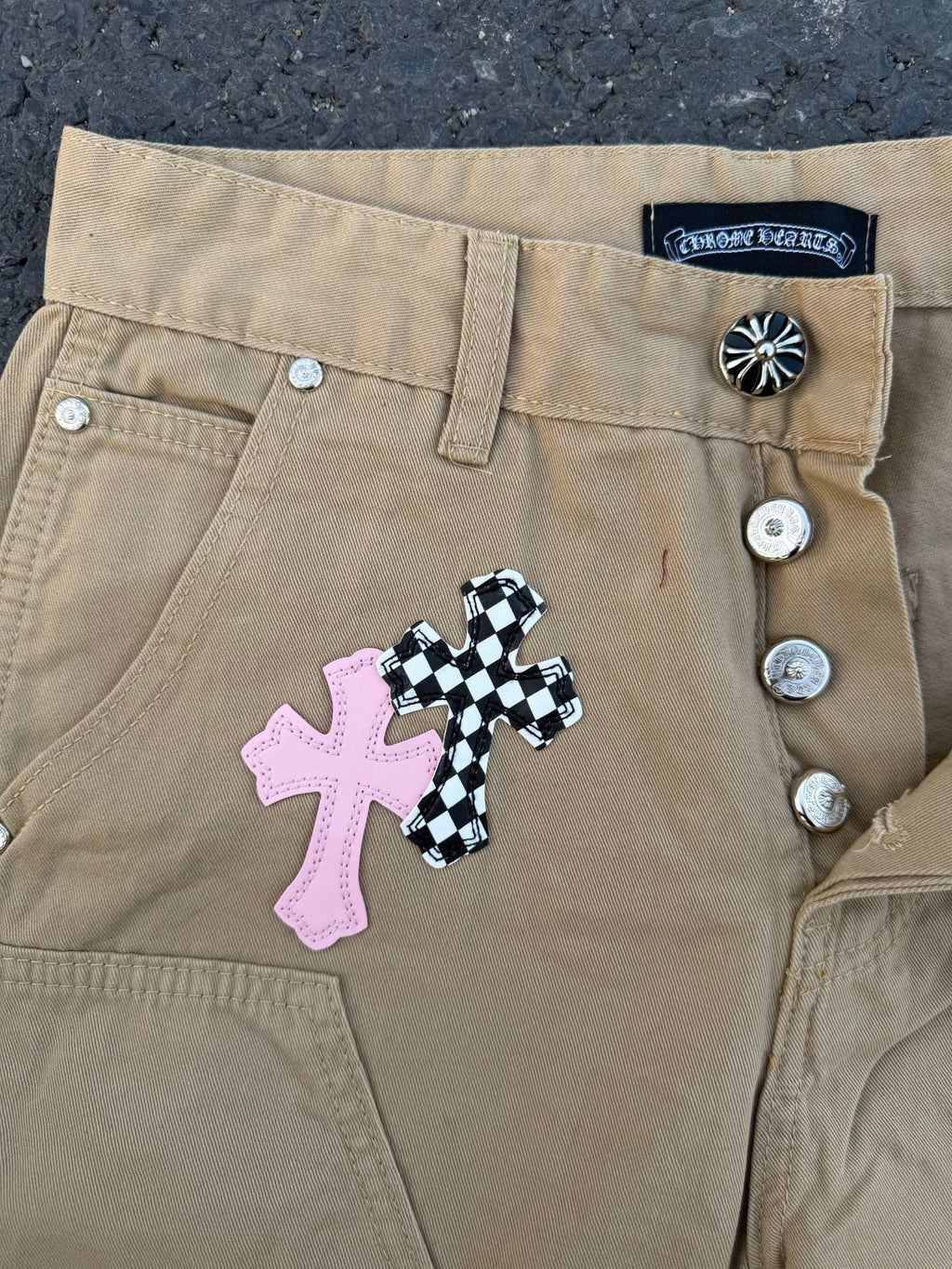 Beige pants close-up of button waistband and cross appliqué patch