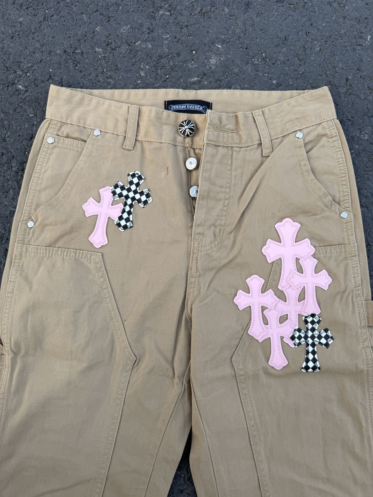 Beige pants front with snap button closure and cross appliqué patches