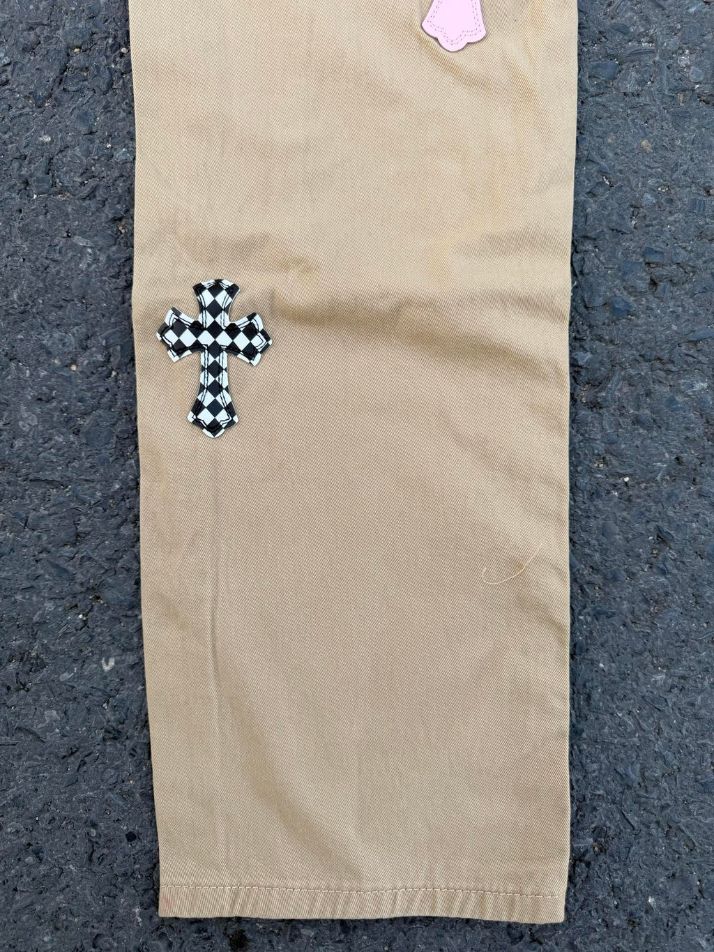 Beige pants with black-checkered cross applique on lower leg