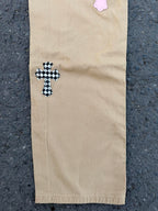 Beige pants with black-checkered cross applique on lower leg