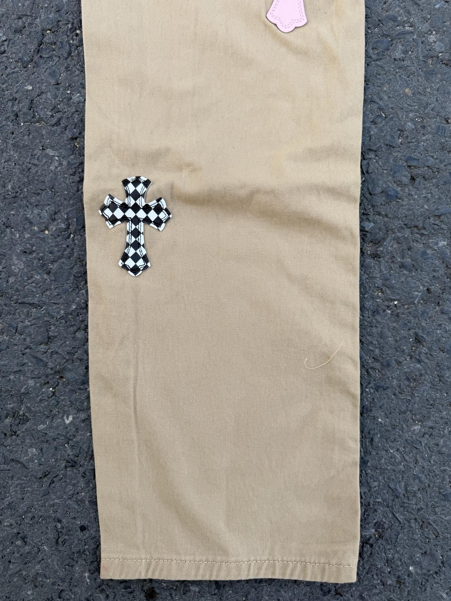 Beige pants with black-checkered cross applique on lower leg