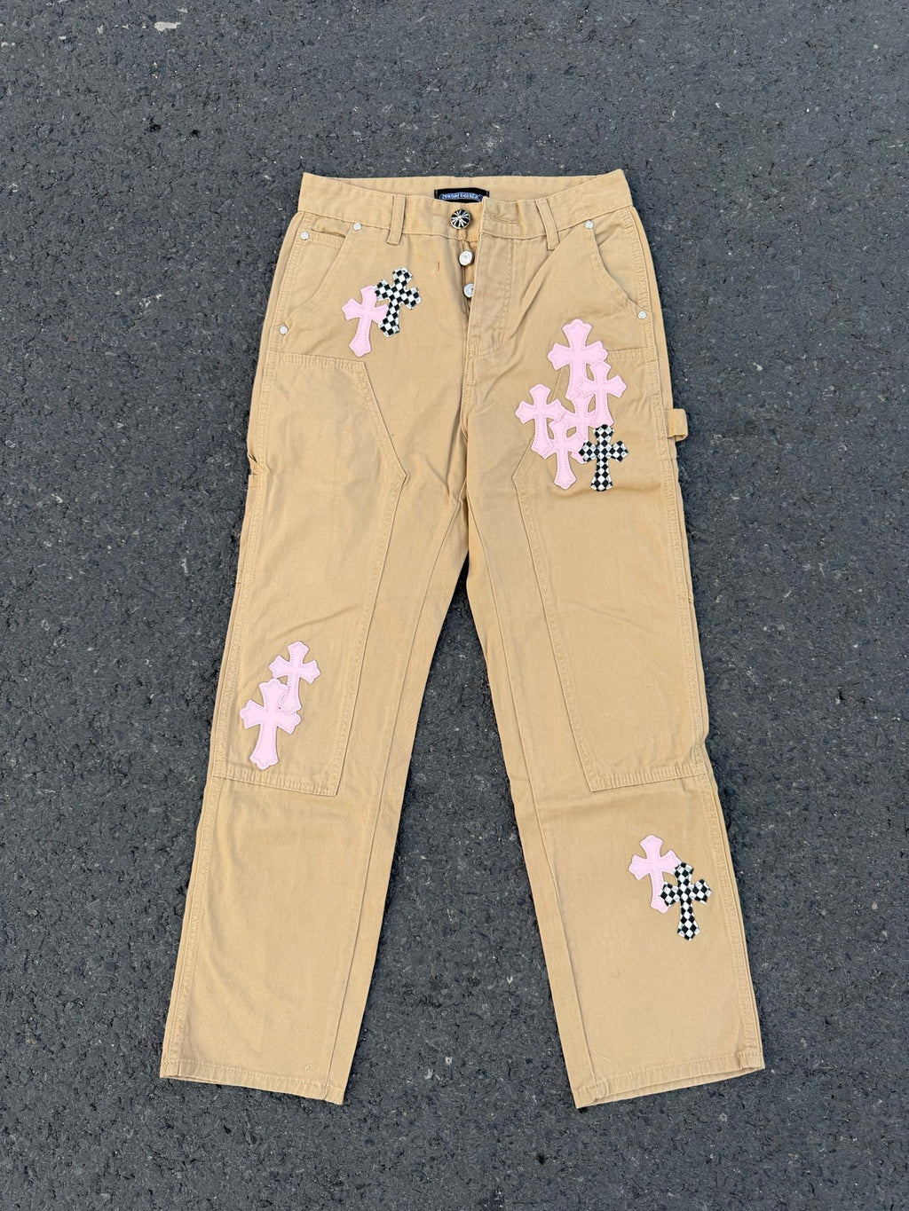 Beige cargo pants with embroidered cross patches and snap fly front