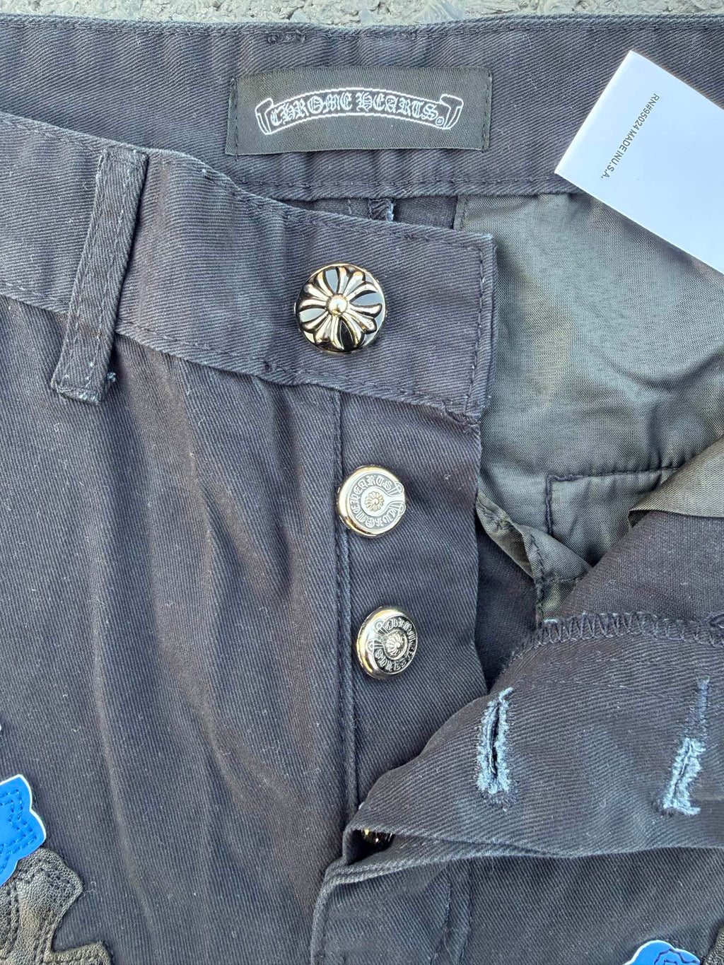 Dark gray pants close-up of waistband label, metal snaps, and stitched hem detail