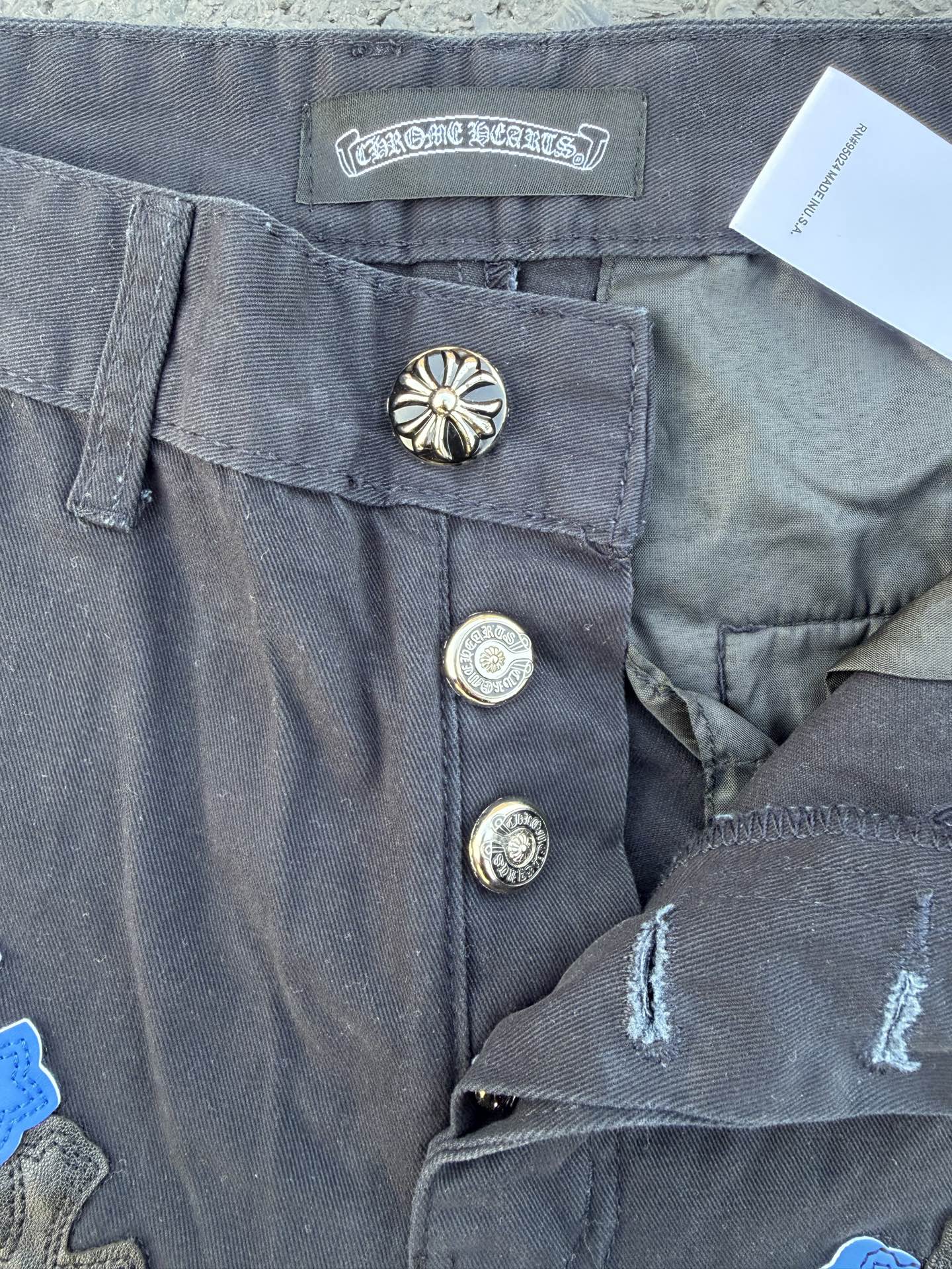 Dark gray pants close-up of waistband label, metal snaps, and stitched hem detail