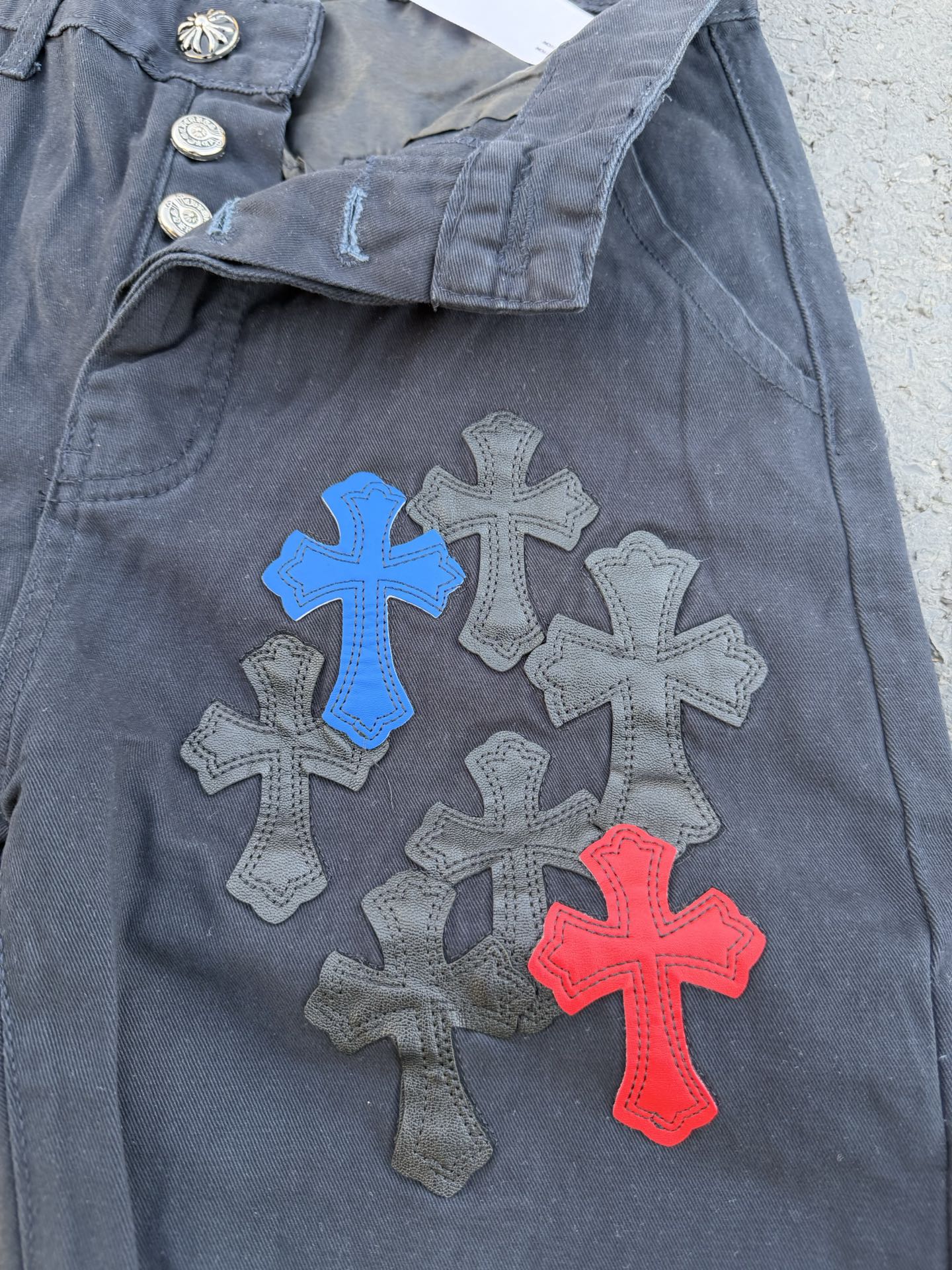 Dark gray pants close-up with belt loop and colorful cross applique on knee
