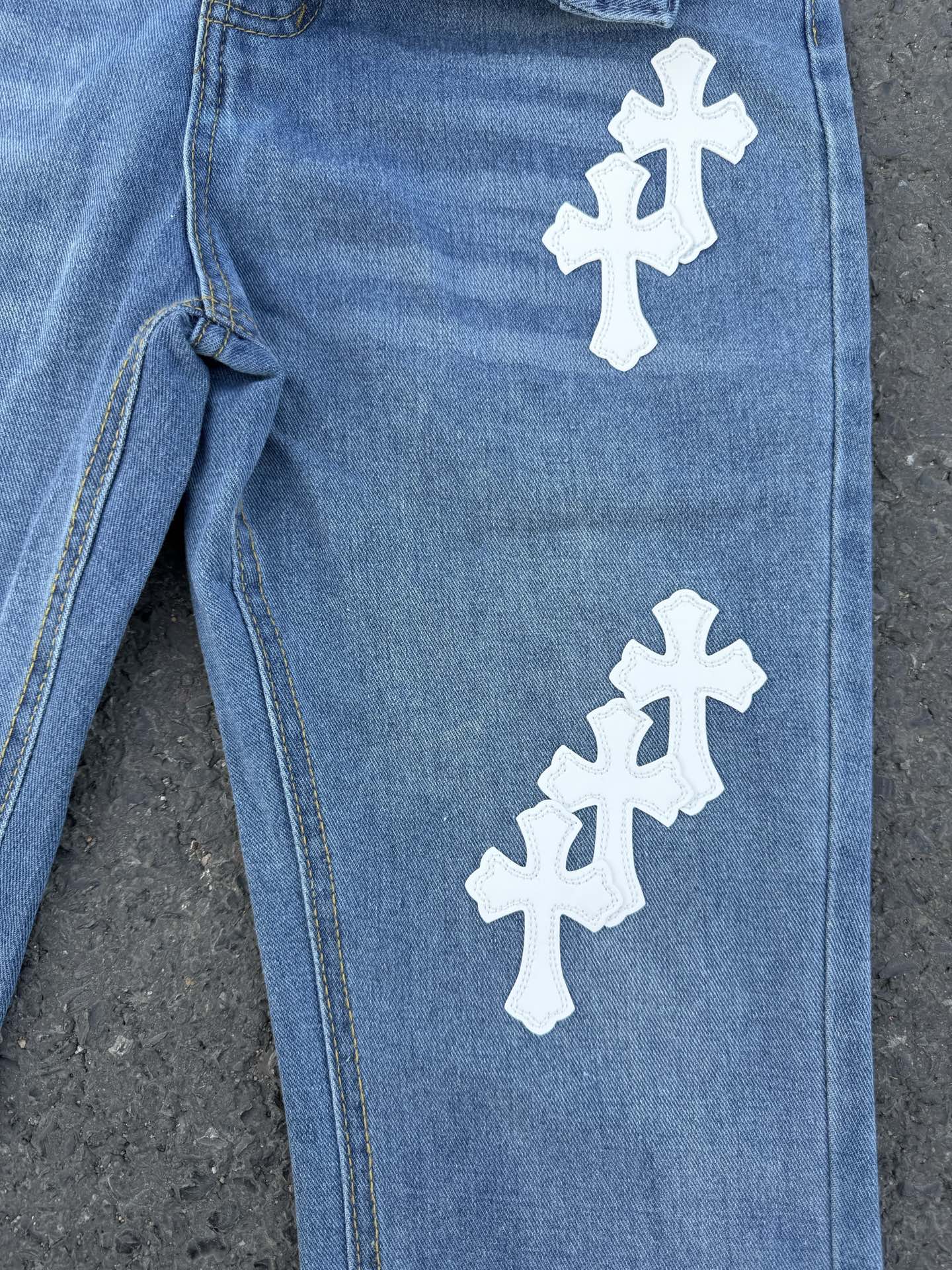 Light blue denim jeans with white cross patches along the leg, side seam detail.