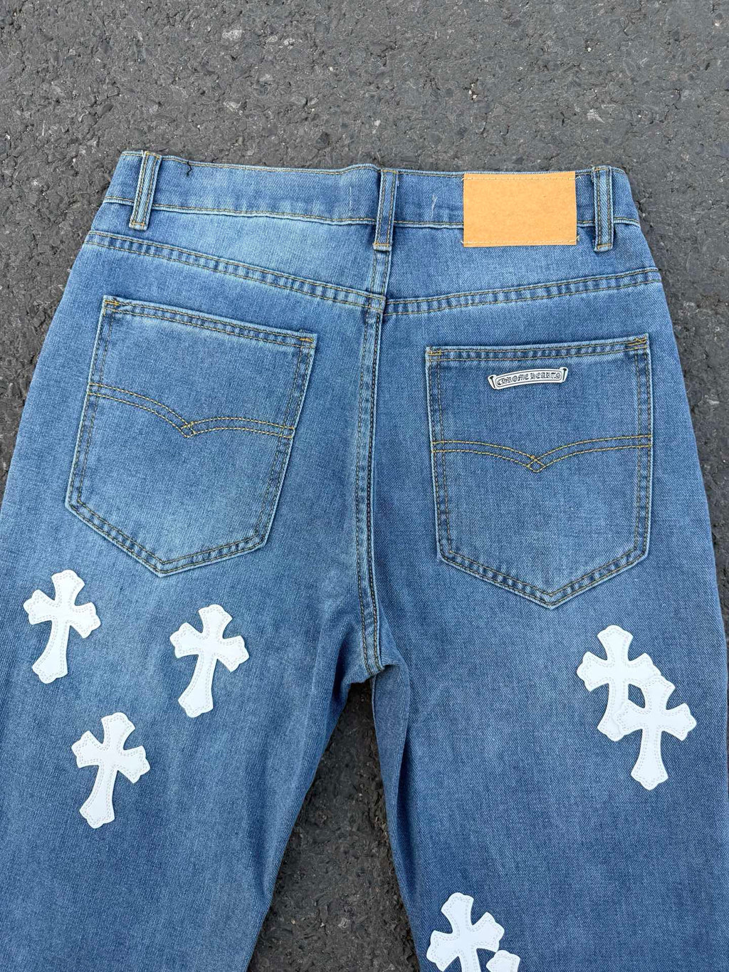 Light blue denim jeans back view with patch pockets and white cross patches.