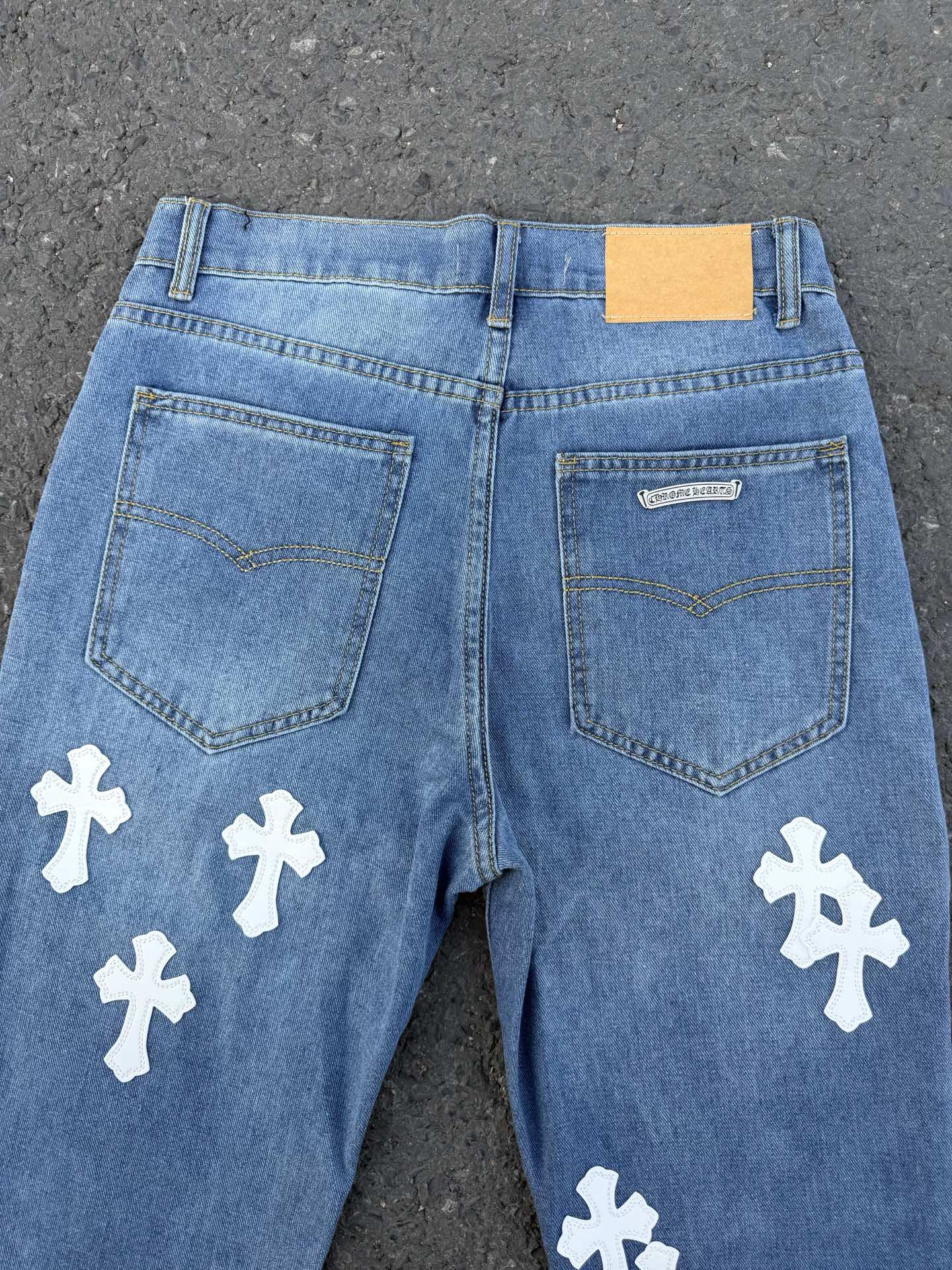 Light blue denim jeans back view with patch pockets and white cross patches.