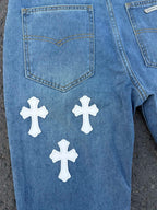 Light blue denim jeans with heart-shaped pocket and white cross graphics.