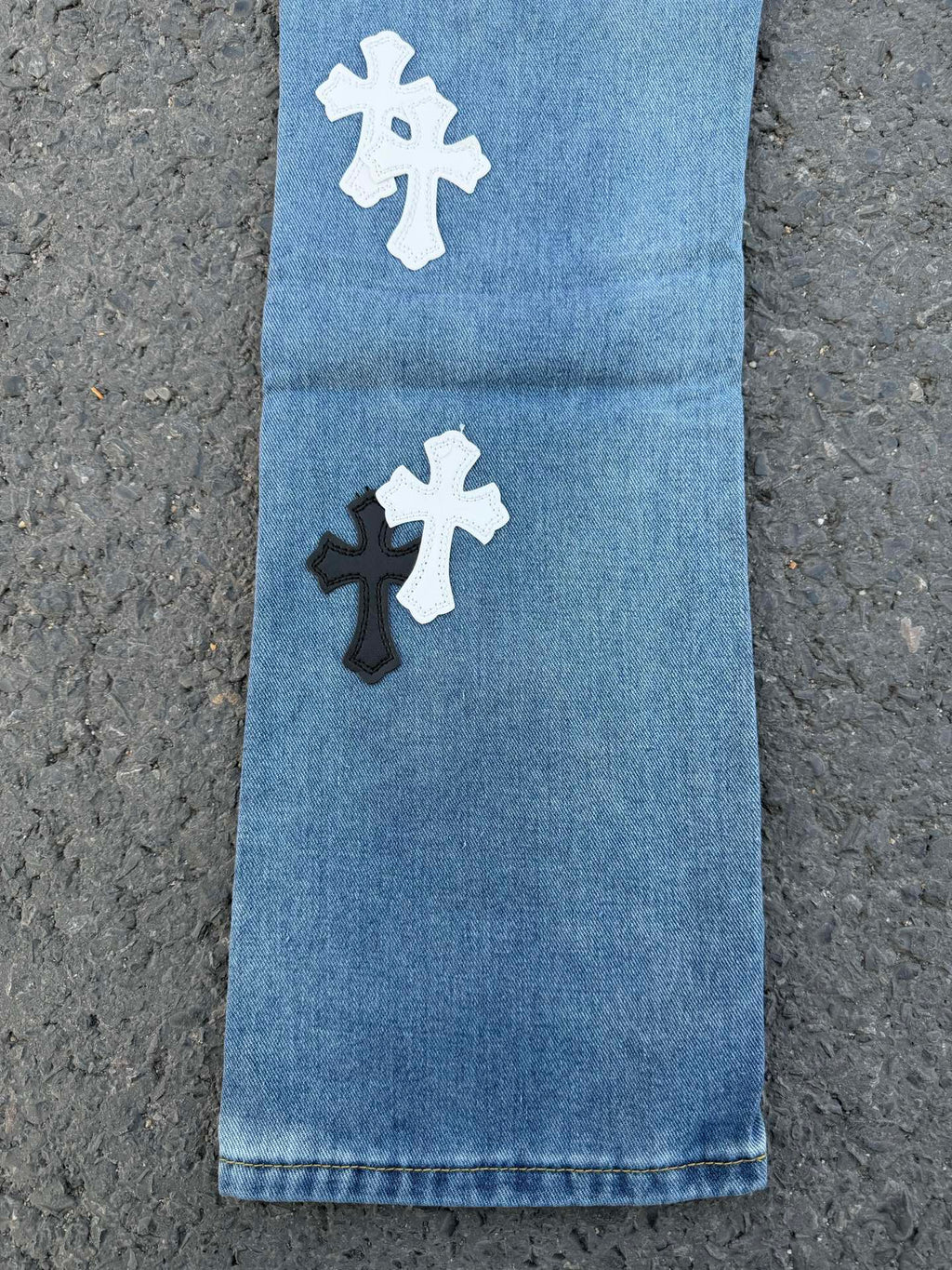 Light blue denim pants with white and black cross patches on the front