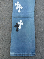 Light blue denim pants with white and black cross patches on the front