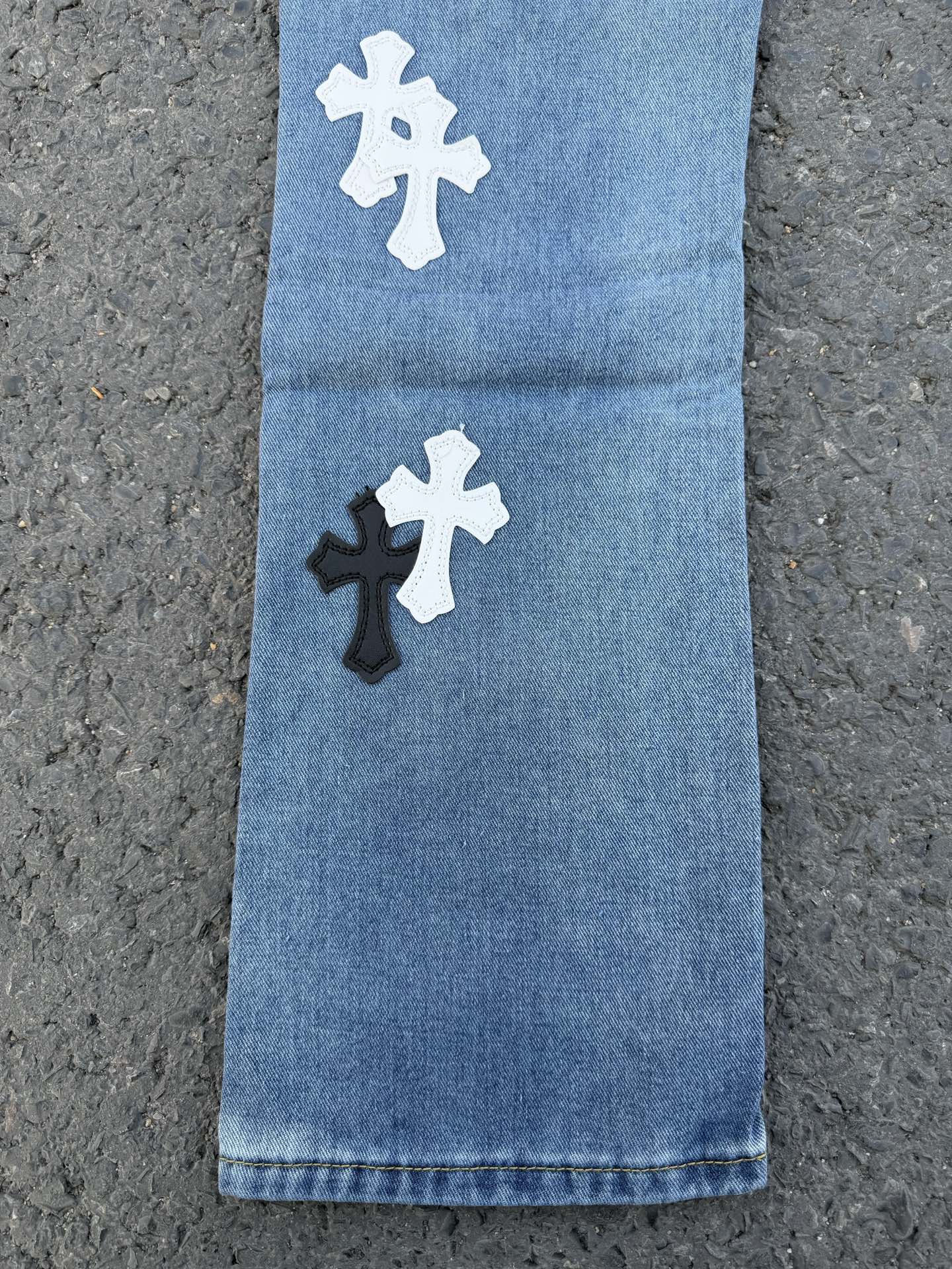 Light blue denim pants with white and black cross patches on the front