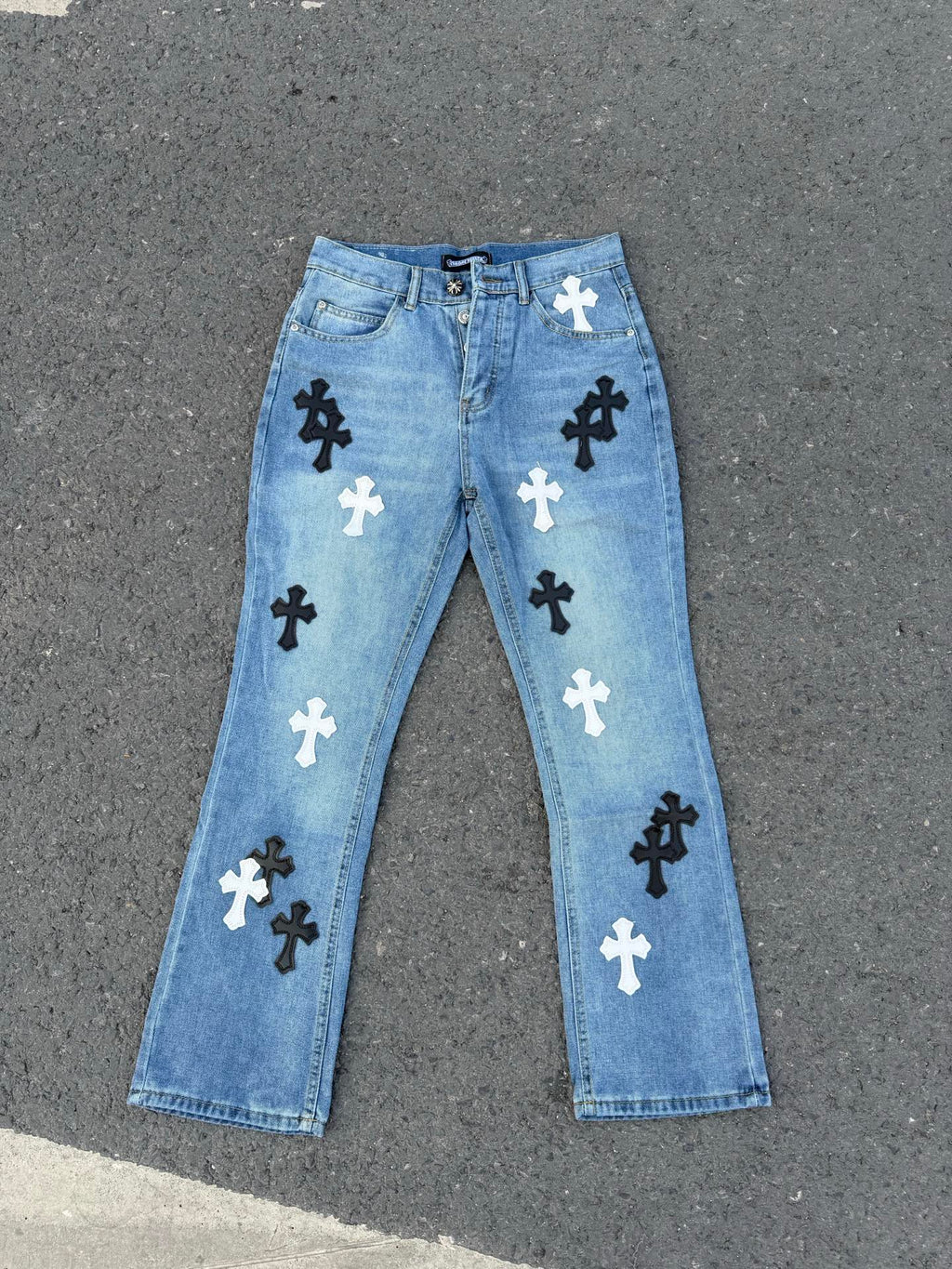 Light blue denim pants with black and white cross patches and button fly