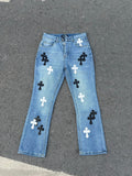 Light blue denim pants with black and white cross patches and button fly