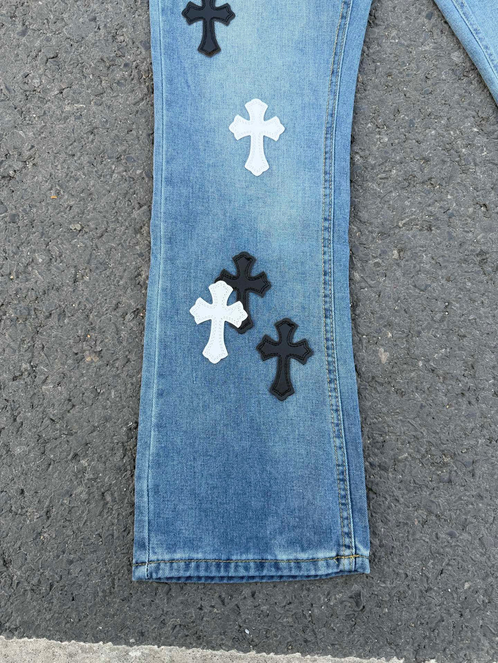 Light blue denim pants with black and white cross patches near the hem
