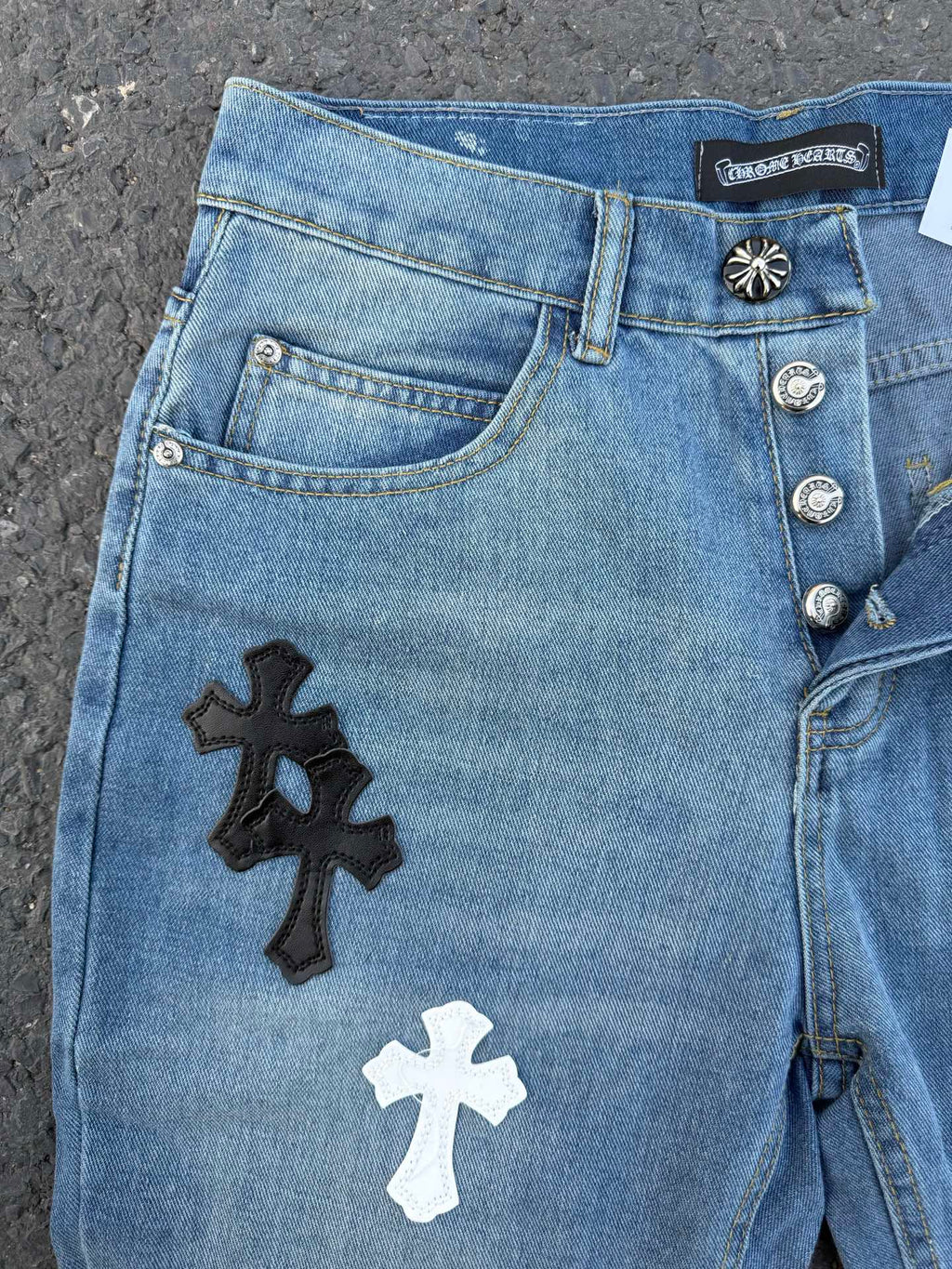 Light blue denim pants with black and white cross patches on the front leg