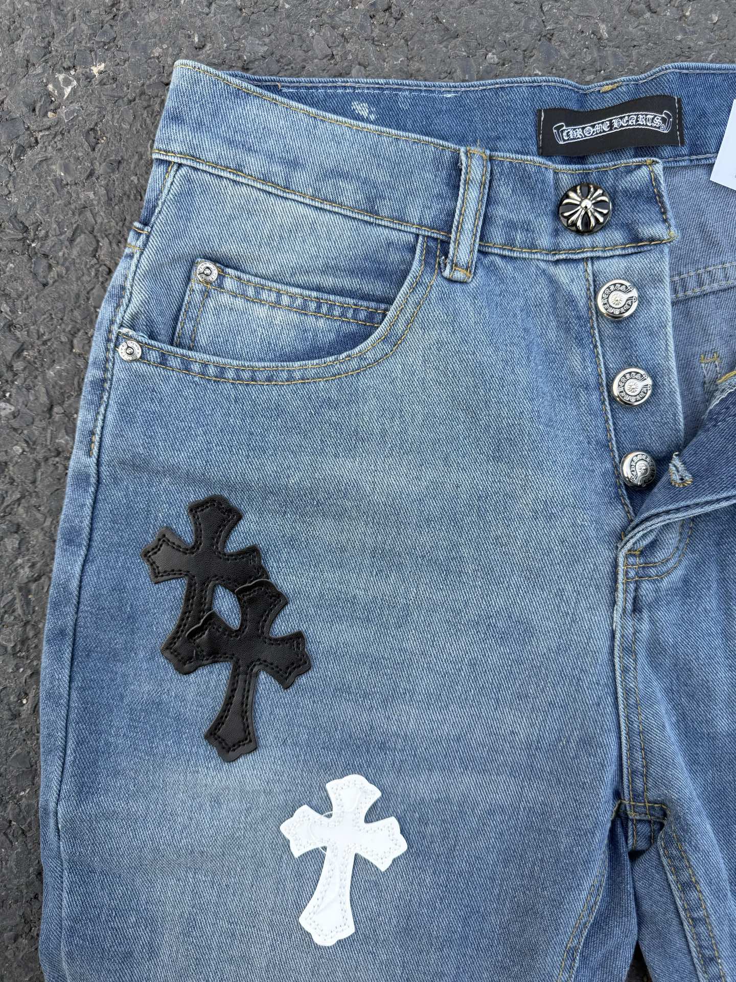 Light blue denim pants with black and white cross patches on the front leg