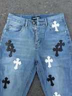 Front view of light blue denim pants with black and white cross applique