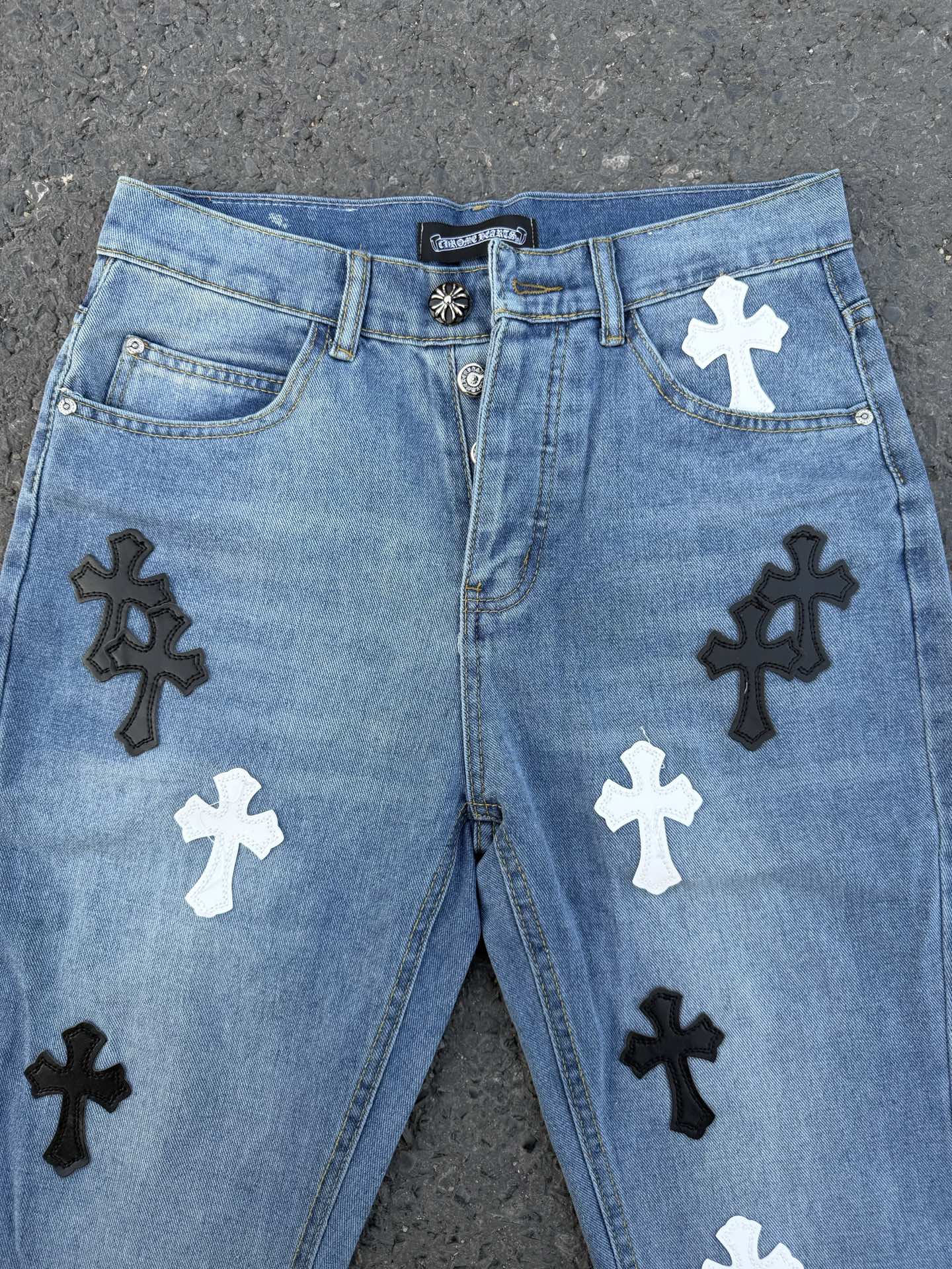 Front view of light blue denim pants with black and white cross applique