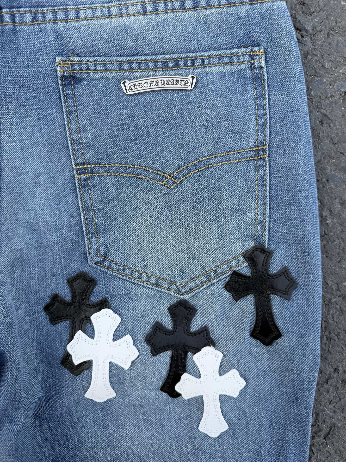 Back pocket of light blue denim pants with label and cross patches below